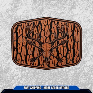 May include: A brown and black rectangular patch featuring a deer skull with crossed arrows. The patch has a textured background and a black border. The text "FAST SHIPPING - MORE COLOR OPTIONS" is at the bottom.
