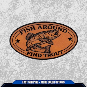 May include: An oval-shaped, orange sticker with a black border and the text "FISH AROUND FIND TROUT". The sticker features a detailed illustration of a trout fish, with two black stars on either side. The background is a textured, light gray.