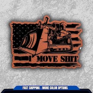 May include: An orange and black patch featuring a bulldozer silhouette set against an American flag design. The text "I MOVE SHIT" is prominently displayed below the bulldozer. The patch has a distressed, weathered look.