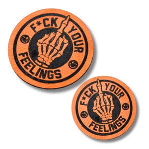 May include: Two orange round patches with black text and a skeleton hand giving the middle finger. The text around the edge says "F*CK YOUR FEELINGS" with a smiley face on each side of the hand.