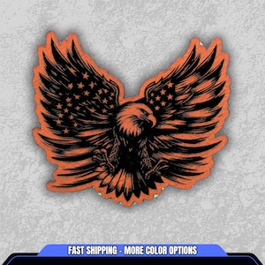 May include: An orange and black graphic of an eagle with outstretched wings. The eagle's wings feature a design of the American flag, with stars and stripes. The image is on a light gray background. The text "FAST SHIPPING - MORE COLOR OPTIONS" is at the bottom.