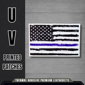May include: A rectangular patch featuring a distressed American flag design with a blue line. The flag has black and white stripes and white stars on a black background. The text "U V PRINTED PATCHES" is on the left side.