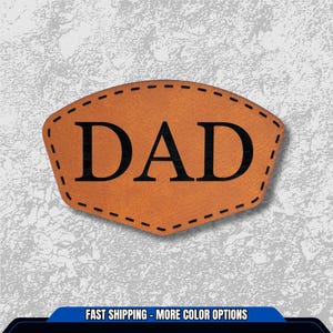 May include: A brown leather patch with the word "DAD" in bold black letters. The patch has a unique shape with a stitched border and is set against a textured gray background.