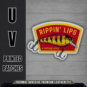 May include: A sticker with a fishing lure design. The sticker has a red and yellow background with the words "RIPPIN' LIPS" and "TAKING SIPS". The lure is yellow and orange with black stripes and silver hooks. The text "PRINTED PATCHES" is also visible.