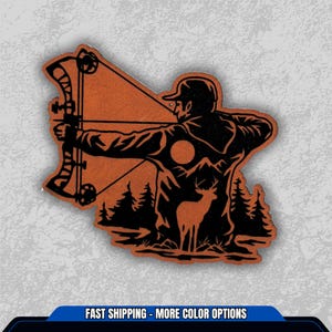 May include: A brown and black patch featuring a silhouette of a person aiming a bow and arrow. The design includes a deer, trees, and a sun, with the text "FAST SHIPPING - MORE COLOR OPTIONS" at the bottom.