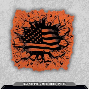 May include: Orange and black graphic of the American flag bursting through a cracked surface. The flag design features stars and stripes. The image has a distressed, textured appearance.