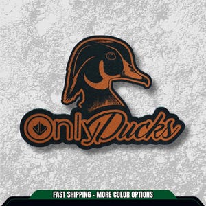 May include: A black and orange sticker featuring a duck illustration. The duck is depicted in profile with detailed feathers and a prominent beak. The text "Only Ducks" is written in an orange, stylized font below the duck.