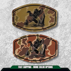May include: Two oval-shaped patches with a camouflage pattern background. Each patch features a black and white illustration of a duck taking flight over water. The patches have a black border. The text "FAST SHIPPING - MORE COLOR OPTIONS" is at the bottom.