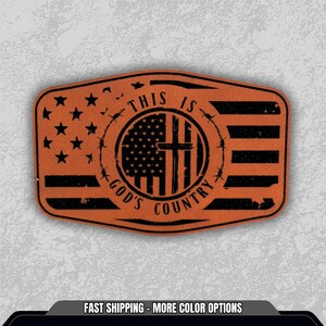 May include: A rectangular, orange-brown patch with a black design. The design includes the American flag, a cross, barbed wire, and the text "THIS IS GOD'S COUNTRY". Stars and stripes are visible.