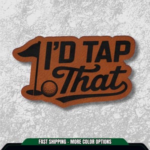 May include: A brown leather patch with the text "I'D TAP THAT" in black lettering. The design includes a golf ball, a flag, and a golf hole. The patch is designed for golf enthusiasts.