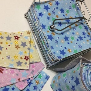Op de afbeelding: Een set herbruikbare make-up remover pads in verschillende kleuren en patronen. De pads zijn gemaakt van zacht, absorberend materiaal en hebben een sterrendruk. De pads worden bewaard in een metalen houder.
