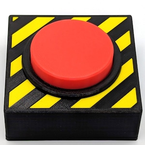 Può includere: Un pulsante rosso con un bordo nero e giallo a strisce. Il pulsante è montato su una base nera.