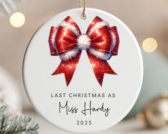 May include: A white ceramic Christmas ornament featuring a red bow with glitter accents and white trim. The text reads "LAST CHRISTMAS AS Miss Hardy 2025". The ornament hangs from a gold string.