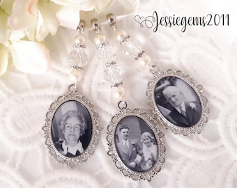 May include: Three silver-toned photo charms with black and white photos of people. Each charm has a delicate, ornate design and is attached to a white beaded string.