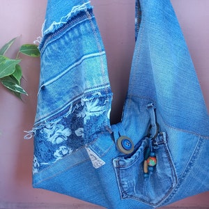 Könnte beinhalten: Eine blaue Jeans-Tragetasche mit einem Blumenmuster und einer kleinen Tasche. Die Tasche hat einen ausgefransten Rand und einen Knopfverschluss.