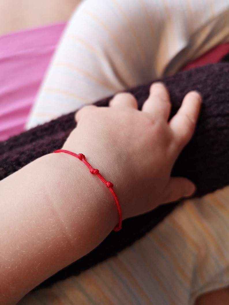 May include: A red string bracelet with small beads on a child's wrist.