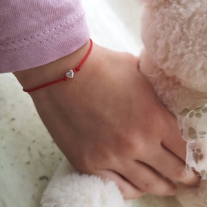May include: A red string bracelet with a small silver heart charm.