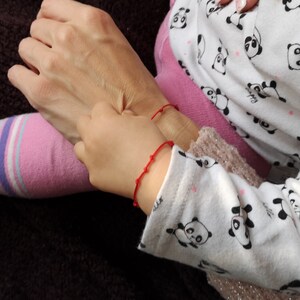 May include: Two people wearing red string bracelets on their wrists. The person on the left is wearing a pink and white striped sock. The person on the right is wearing a white shirt with black panda bears printed on it.