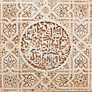 Könnte beinhalten: Eine weiße Fliese mit aufwendigen Schnitzereien von geometrischen Mustern und arabischer Schrift. Die Fliese ist von einem Rand aus kleineren geometrischen Mustern umgeben.