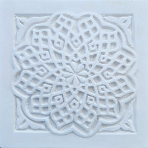 May include: White ceramic tile with an intricate, carved, geometric design. The design is symmetrical and resembles a flower with multiple layers of petals.