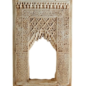 May include: A rectangular, off-white, carved stone archway with intricate geometric and calligraphic designs. The arch features a central opening and detailed relief patterns, showcasing a traditional architectural style.