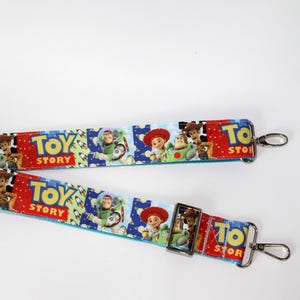 Puede incluir: Una correa azul y blanca con tem&aacute;tica de Toy Story con im&aacute;genes de Woody, Buzz Lightyear y Jessie. La correa tiene cierres met&aacute;licos plateados y las palabras "Toy Story" en rojo y amarillo.