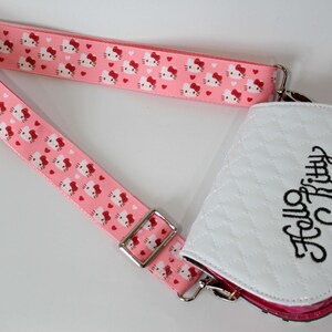 Puede incluir: Un bolso bandolera rosa con una correa a juego con un patr&oacute;n repetido de caras y corazones de Hello Kitty. El bolso tiene una parte delantera acolchada blanca con "Hello Kitty" en escritura negra.
