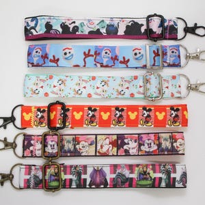 May include: A collection of six colorful lanyards with various cartoon character designs. The lanyards feature images of Mickey Mouse, Disney villains, and other characters. Each lanyard has a metal clasp and buckle.
