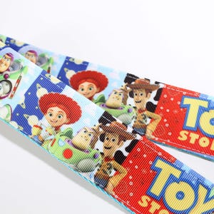 Puede incluir: Dos cintas con un colorido dise&ntilde;o de Toy Story. Una cinta presenta a Buzz Lightyear, Jessie y Woody. La otra cinta tiene el logo de Toy Story en rojo. El fondo incluye cohetes y nubes.