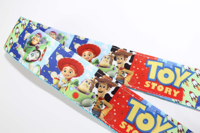 Puede incluir: Dos cintas con un colorido dise&ntilde;o de Toy Story. Una cinta presenta a Buzz Lightyear, Jessie y Woody. La otra cinta tiene el logo de Toy Story en rojo. El fondo incluye cohetes y nubes.