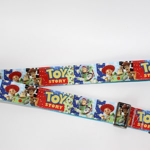 Puede incluir: Dos correas azules y rojas con tem&aacute;tica de Toy Story con cierres met&aacute;licos plateados. Las correas presentan im&aacute;genes de Woody, Buzz Lightyear y otros personajes de la pel&iacute;cula. Las palabras "Toy Story" est&aacute;n impresas en las correas.