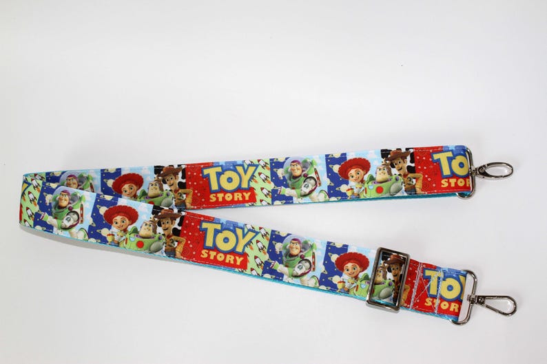 Puede incluir: Dos correas azules y rojas con tem&aacute;tica de Toy Story con cierres met&aacute;licos plateados. Las correas presentan im&aacute;genes de Woody, Buzz Lightyear y otros personajes de la pel&iacute;cula. Las palabras "Toy Story" est&aacute;n impresas en las correas.