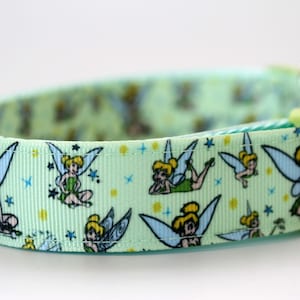 Peut inclure: Un collier pour animal de compagnie vert clair avec un motif répétitif de la fée Clochette dans diverses poses, agrémenté de petites étoiles jaunes et bleues. Le collier comprend une boucle en plastique vert clair et un anneau en métal.