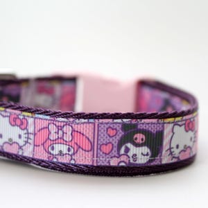 May include: A purple pet collar featuring a repeating pattern of Sanrio characters including Hello Kitty, My Melody, and Kuromi in square frames. The collar includes a light pink plastic side-release buckle and a matching light pink plastic slider.