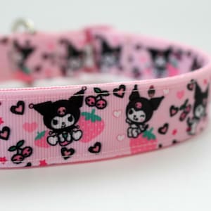 May include: Pink pet collar featuring a repeating pattern of a cartoon character with black ears, strawberries, cherries, and hearts. The collar has a silver metal clasp.