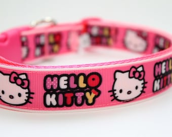 May include: Pink dog collar featuring the text "HELLO KITTY" and the Hello Kitty character. The collar has a white border and a plastic buckle. The design is repeated around the collar.