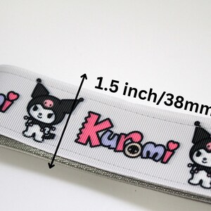 Puede incluir: Cinta gris claro con un patr&oacute;n repetido de un personaje de dibujos animados y la palabra "Kuromi" en rosa y morado. La cinta mide 3,8 cm de ancho.