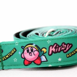 Könnte beinhalten: Eine grüne und rosa Hunde-Leine mit einer Comicfigur von Kirby aus der Videospielserie. Die Leine hat die Worte "Kirby" und "Adventure" aufgedruckt.
