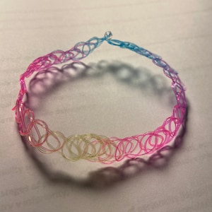 May include: A pink, yellow, and blue plastic choker necklace with a silver clasp.