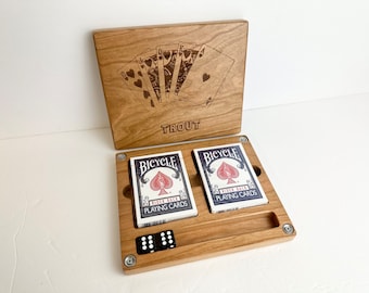 May include: A wooden box with a hinged lid, engraved with a design of playing cards and the word "TROUT". The box is open, revealing two decks of Bicycle playing cards and four dice.