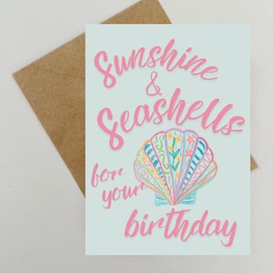 May include: A light blue greeting card with pink cursive text that reads Sunshine & Seashells for your birthday. Below the text is a colorful illustration of a seashell with intricate patterns in blue, pink, yellow, and green. A brown envelope is behind it.