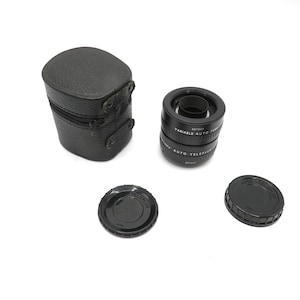 May include: A set of three black lens attachments for a camera. The lenses are labeled "Detay Variable Auto Telephoto" and come in a black leather case.