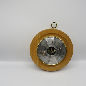 May include: A wooden framed barometer with a silver face and a needle pointing to "Very Dry". The face has markings for "Stormy", "Rain", "Change", "Fair", and "Very Dry".