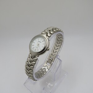K&ouml;nnte beinhalten: Eine silberfarbene Armbanduhr mit wei&szlig;em Zifferblatt und silbernem Armband. Auf dem Zifferblatt der Uhr steht "BERGE" und "QUARTZ".