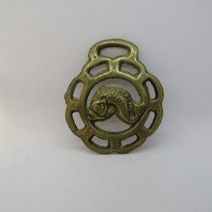 Op de afbeelding: Een gouden metalen paardenhanger met een ingewikkeld ontwerp met een vis in het midden.