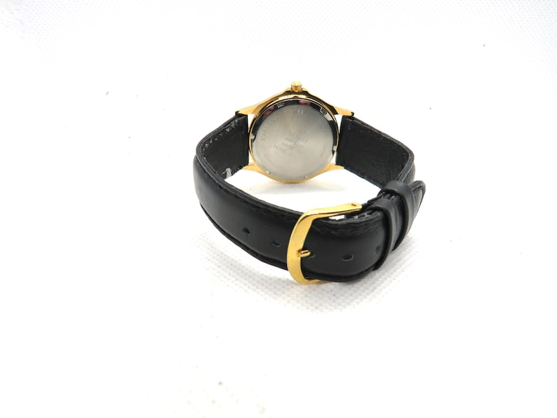 May include: A gold-tone watch with a black leather band. The watch face is silver and has black markings. The watch has a gold-tone buckle.