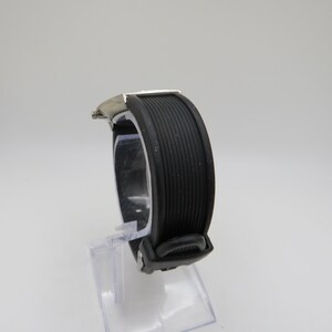 May include: A silver and black wristwatch with a black rubber band. The watch is on a clear display stand.