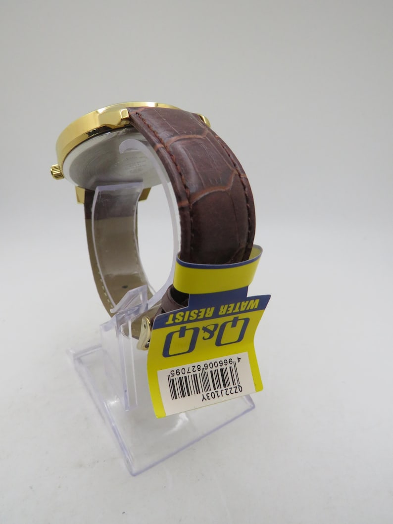May include: A gold-toned wristwatch with a brown leather band. The watch has a round face and a textured band. A yellow tag with the text "WATER RESIST" and the brand "Q&Q" is attached to the watch.