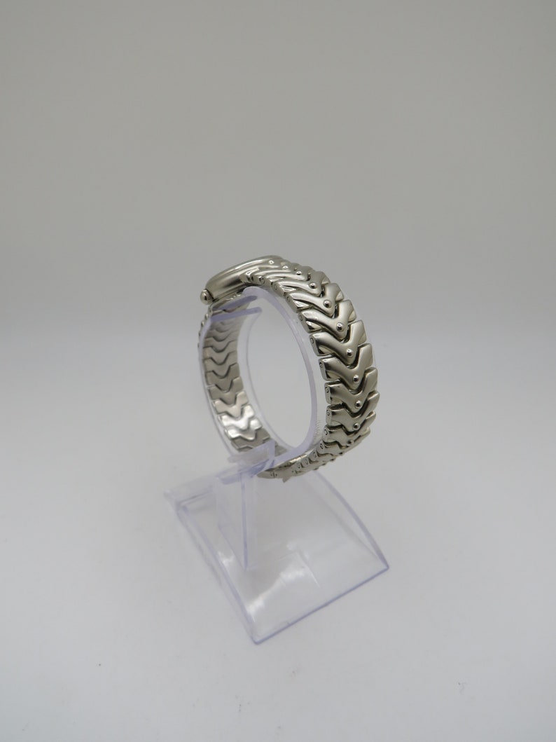K&ouml;nnte beinhalten: Silberfarbenes Armband f&uuml;r eine Uhr mit einem einzigartigen, ineinandergreifenden Chevron-Design.