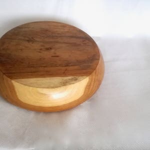 K&ouml;nnte beinhalten: Eine runde Holzschale mit hellbrauner Farbe und einem dunkelbraunen Rand. Die Schale ist aus Naturholz gefertigt und hat eine glatte, polierte Oberfl&auml;che.